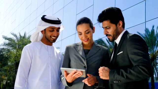 Three business professionals discuss over a tablet outside a modern building, highlighting RAKEZ Free Zone's benefits.