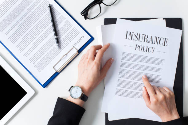 Person reviewing insurance policy documents at a desk with glasses, a contract, tablet, and pen nearby.