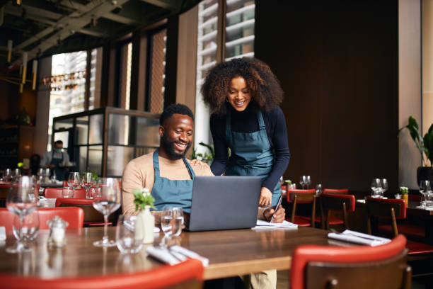 Two small business owners manage multiple projects on a laptop in a cozy café setting.