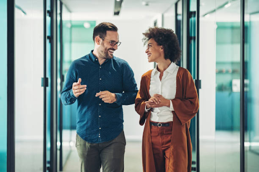 Two professionals discuss business matters while walking through a modern office hallway.